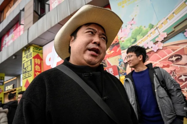 На фотографії, зробленій 15 грудня 2025 року, зображено імітатора Дональда Трампа Раяна Чена, який готується до короткої відеозйомки на вулиці в південно-західному Китаї в муніципалітеті Чунцін. Простягнувши руки у фірмовій позі Дональда Трампа, імітатор Раян Чень так точно імітує голос і жестикуляцію президента США, що завдяки своїм кумедним відео він став феноменом соціальних мереж. (Фото Джейд Гао / AFP через Getty Images) / ДЛЯ: Китай-США-соціальна-комедія-Трамп, ПРОФІЛЬ Людовіка ЕРЕТА