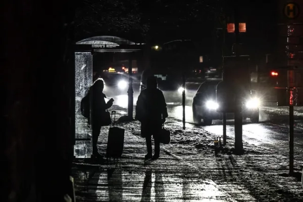 Люди чекають на автобусній зупинці на темній вулиці західного Берліна, Німеччина, 3 січня 2026 року. На початку 3 січня у західному Берліні сталося серйозне відключення електроенергії після того, як загорівся кабельний міст через Тельтовський канал, пошкодивши лінії електропередач. Пожежники загасили полум'я, а поліція розслідує можливий підпал.