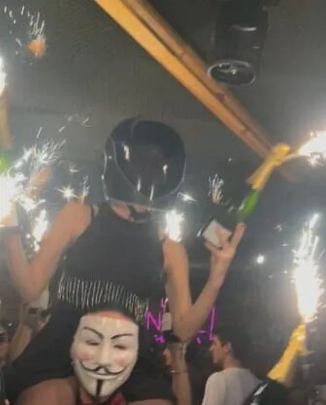 Ось фотографія, зроблена БЕЗПОСЕРЕДНЬО ДО спалаху пожежі, яка сталася в барі в Кран-Монтані, забравши життя щонайменше 40 людей та поранивши понад 115, більшість з яких отримали серйозні поранення. На ній зображена офіціантка, яку підняли на плечі, тримаючи пляшки шампанського з ІГРИСТИМИ СВІЧКАМИ, безпосередньо біля стелі, яка загорілася лише через кілька секунд.