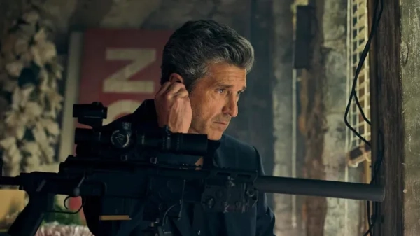 Патрік Демпсі носить чорну куртку та стоїть за величезною рушницею.