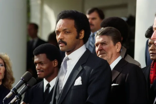 Правозахисник Джессі Джексон виступає під час церемонії на честь пілота ВМС Роберта О. Гудмена (ліворуч), якого збили та взяли в полон у Сирії. Президент Рональд Рейган (праворуч) слухає. (Фото Ларрі Даунінга/Sygma/Sygma через Getty Images)