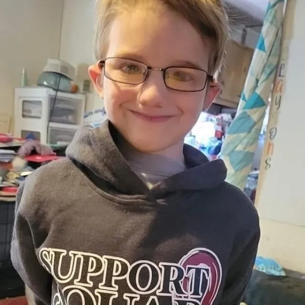 Середній крупний план фотографії хлопчика-підлітка, який посміхається, носить окуляри та одягнений у сіру толстовку з капюшоном.