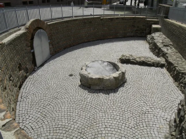 МАРК ВОРГАН Археологи, які працюють під історичним центром Кельна, виявили надзвичайно добре збережені римські залишки, зокрема рідкісну святиню домашніх богів, знайдену вперше в Північній Європі. За словами міських чиновників, знахідку було зроблено під час розкопок, пов'язаних з новим підземним маршрутом для відвідувачів у Єврейському музеї MiQua ??? LVR в Археологічному кварталі Кельна. Найбільш вражаючим відкриттям є ларарій – домашнє святилище, присвячене ларам, божествам-захисникам дому, – знайдене в колишньому римському преторії, палаці губернатора, який колись символізував імператорську владу в провінції Нижня Германія. Ларії були широко поширені в римських будинках по всьому Середземномор'ю. Цей, що датується II століттям, є унікальним на північ від Альп, а аналогічні приклади раніше знаходили лише в римських містах, похованих внаслідок вивержень вулканів, таких як Помпеї. Команда дослідників, яка брала участь у розкопках, каже, що кельнська знахідка майже безпрецедентна: сліди оригінального настінного розпису досі видно всередині вівтарної ніші. Невеликі отвори від цвяхів над і поруч із нішею свідчать про те, що колись святиню прикрашали гірлянди. Під ним чітка лінія розриву позначає місце, де спочатку був встановлений вівтарний стіл. Цю кам'яну плиту також було виявлено під час розкопок, і очікується, що її буде відновлено у початковому положенні. Відкриття були зроблені під час робіт, що проводилися містом Кельн у рамках підготовки до підземної екскурсії музею. Оскільки ділянки нового маршруту опускаються на незвичайну глибину, археологи змогли ідентифікувати споруди, які зазвичай втрачаються, будучи зруйнованими пізнішими будівельними роботами. У цьому випадку останки збереглися, оскільки вони вже були поховані в римські часи. Їхнє розташування на та під колишнім схилом річки Рейн означало, що вони були запечатані валами на початку античності, захищаючи їх від пізніших пошкоджень. Серед інших значущих знахідок - фундамент апсиди, що належить до великої багатонефної римської базиліки, що датується IV століттям. Її товщина досягала чотирьох метрів, і спочатку вважалося, що вона була зроблена з римського литого бетону, відомого як opus caementicium. Детальне дослідження виявило замість цього шарувату конструкцію з туфу, базальту та вапняку, скріплену надзвичайно міцним розчином з цегли та гравію. До розкопок споруда виглядала на площі ратуші Кельна лише як невелике заглиблення. Зараз вона вперше доступна для відвідувачів. Археологи також виявили сходи кінця I століття, які були виявлені лише під час поточних робіт. Сходи колись з'єднували низовину поблизу Рейну з вищою місцевістю, пов'язаною з раннім преторієм. Точна точка, де закінчувалися сходи, залишається невідомою. Сходи рідко зберігаються в археології Кельна, оскільки більшість римських будівель збереглися лише на рівні фундаменту. Фахівці кажуть, що цей екземпляр зберігся завдяки сприятливим топографічним умовам, коли ранні римські споруди були поховані під час засипання ще в римський період. Очікується, що знахідки стануть центральною частиною підземної екскурсії, коли музей MiQua відкриється для публіки. У розділі: Вид на апсиду до початку розкопок. Де: Кельн, Німеччина Коли: 24 лютого 2026 р. Авторство: Місто Кельн/Римсько-германський музей, Міхаель Віен/Зображення обкладинки **З усіх питань використання та запитів звертайтеся за адресою info@cover-images.com - +44 (0)20 3397 3000 ЛИШЕ ДЛЯ РЕДАКЦІЙНОГО ВИКОРИСТАННЯ. МАТЕРІАЛИ ДЛЯ ВИКОРИСТАННЯ ЛИШЕ РАЗОМ З РЕДАКЦІЙНОЮ СТАТТЮ. ВИКОРИСТАННЯ ЦИХ МАТЕРІАЛІВ ДЛЯ РЕКЛАМИ, МАРКЕТИНГУ АБО БУДЬ-ЯКИХ ІНШИХ КОМЕРЦІЙНИХ ЦІЛЕЙ СУВОРО ЗАБОРОНЕНО. АВТОРСЬКЕ ПРАВО НА МАТЕРІАЛИ ЗАЛИШАЄТЬСЯ У ЗАЯВЛЕНОГО ПОСТАЧАЛЬНИКА.**