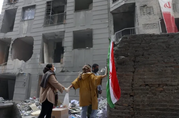 epa12821165 Іранські сестри тримаються за руки, стоячи перед своїм пошкодженим житловим будинком на півдні Тегерана, Іран, 15 березня 2026 року. Спільна військова операція Ізраїлю та США, спрямована проти кількох місць по всьому Ірану, триває з ранку 28 лютого 2026 року. EPA/ABEDIN TAHERKENAREH