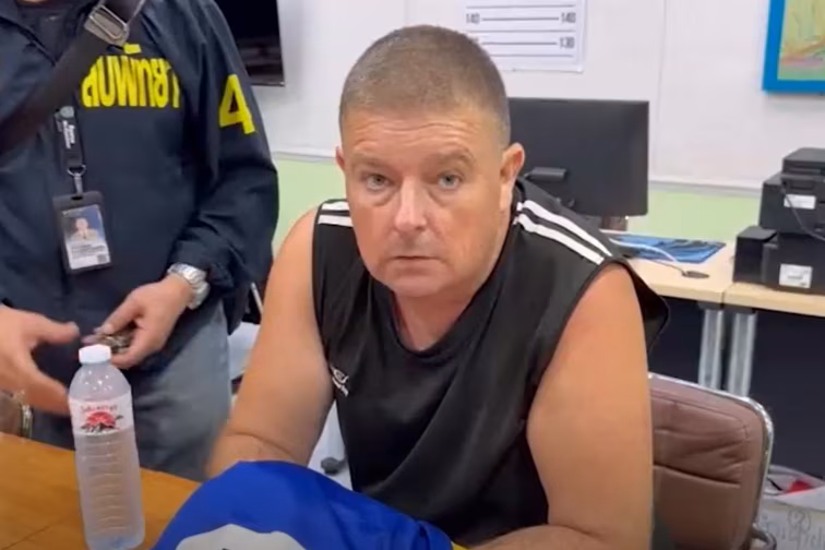 Чоловік сидить у футболці за столом, дивлячись у камеру.