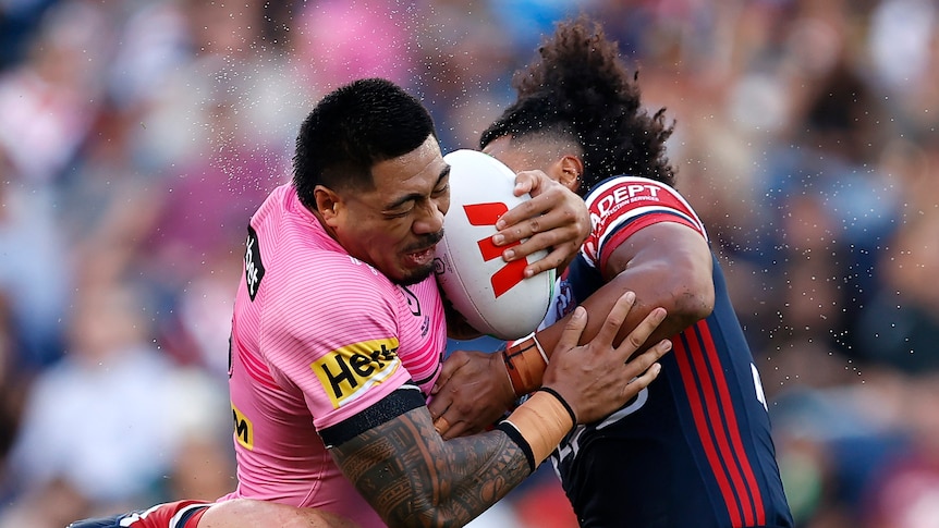Rugby league player in pink gets tackled by a player in blue and red