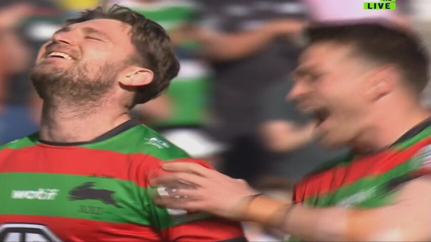 Jai Arrow, wearing a Rabbitohs jersey, looks up and smiles in an emotional way