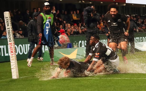 Damian McKenzie scores a try in wet conditions.