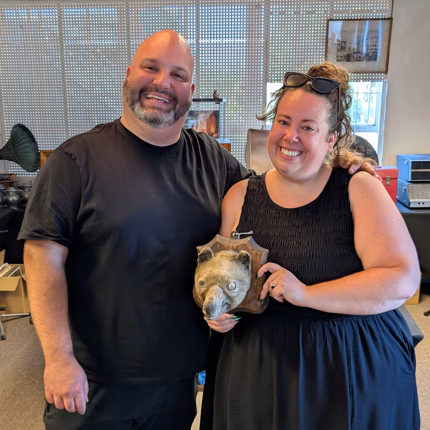 A man and a woman hold a mounted taxidermy animal head that resembles a thylacine, or Tasmanian tiger. 