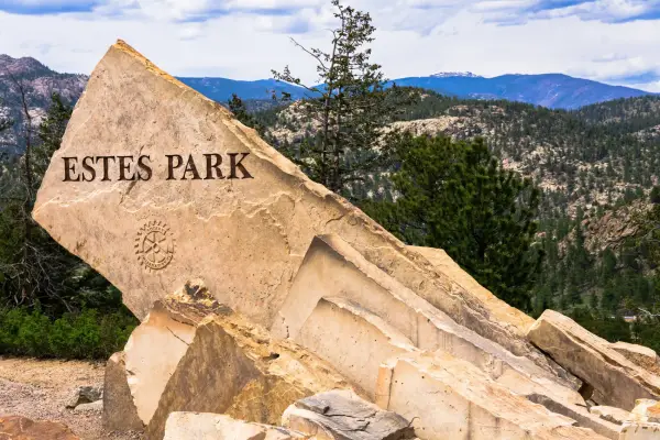 Estes Park, CO - USA - May 29th 2023: Estes Park entrance sign, crafted on a slanted rock, stands proudly amid pine trees with the majestic Colorado mountains as a backdrop.; Shutterstock ID 2407710241; purchase_order: -; job: -; client: -; other: