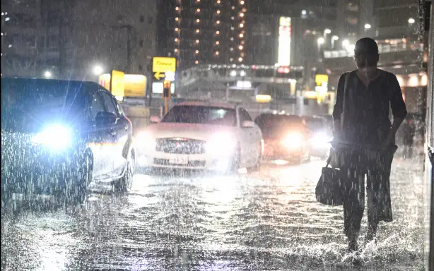 Cars pass a commuter on a flooded road near Chiba metro station in Chiba on August 13, 2026, as heavy rain swept through the area. Torrential rain pummelled eastern Japan, triggering landslides and power outages, and prompting the weather authority to issue its highest-level heavy rain warning for the region for the first time. (Photo by Philip FONG / AFP)