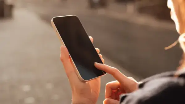 Жіноча рука, що гортає смартфон, на задньому плані розмитий міський пейзаж у теплому сонячному світлі. Зв'язок і присутність у сучасному міському житті. Концепція людського дотику, технологій та повсякденної рутини.