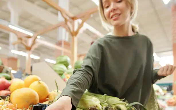 Жінка тягнеться, щоб взяти помідор у відділі продуктів супермаркету.