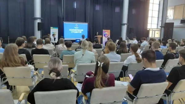 Дівчина за трибуною біля екрану виступає перед людьми в залі (більш загальний план)