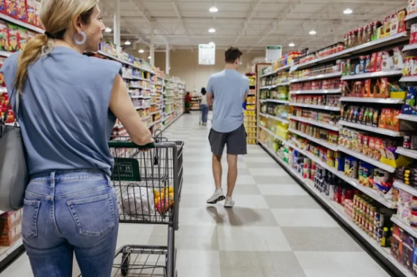 Woman grocery shopping, pushing a cart down a supermarket aisle. Casual attire, modern store interior. Concepts: consumerism, shopping, lifestyle, everyday life.